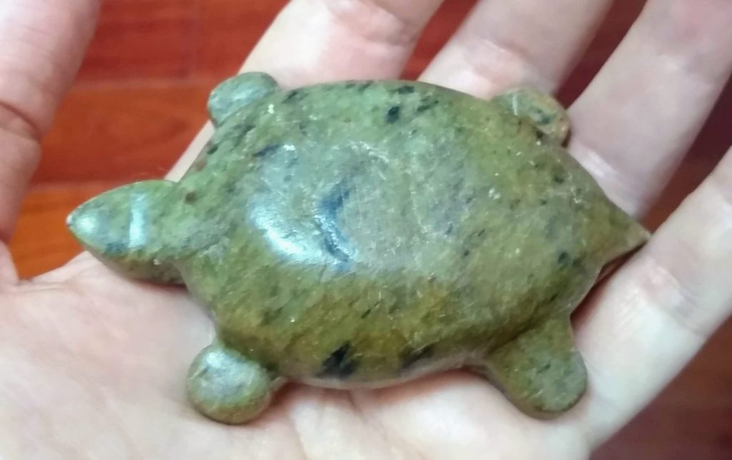 A soapstone turtle, somewhat featureless, sitting in the palm of a light-skinned hand
